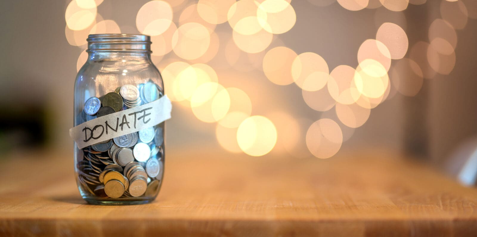 Jar full of coins for donation on wooden desk with blurred background