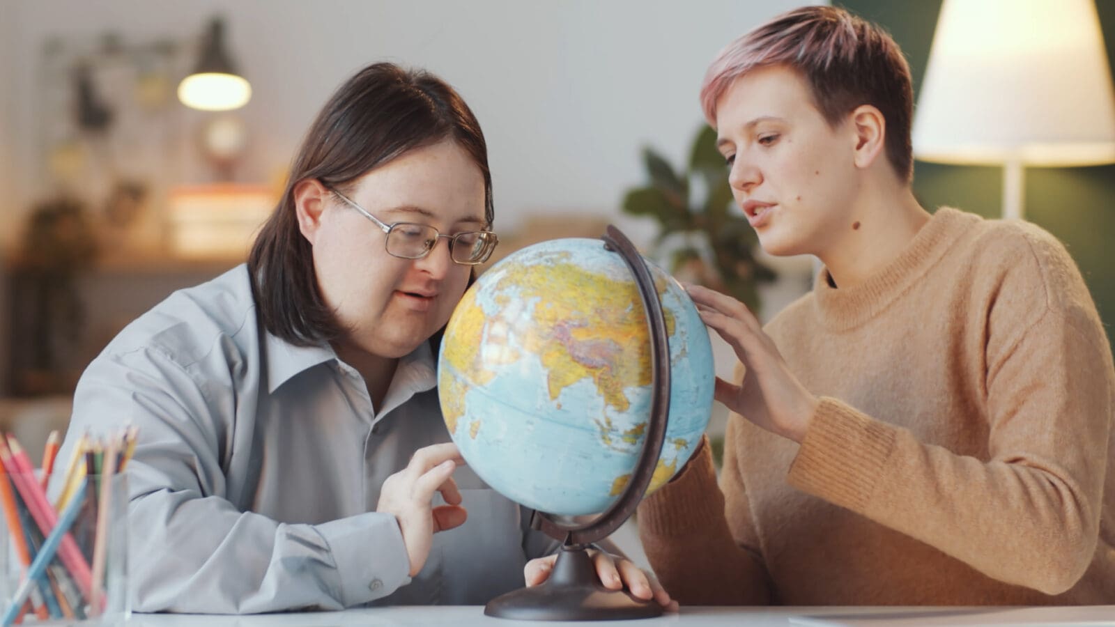 Down syndrome adult and teacher looking at globe
